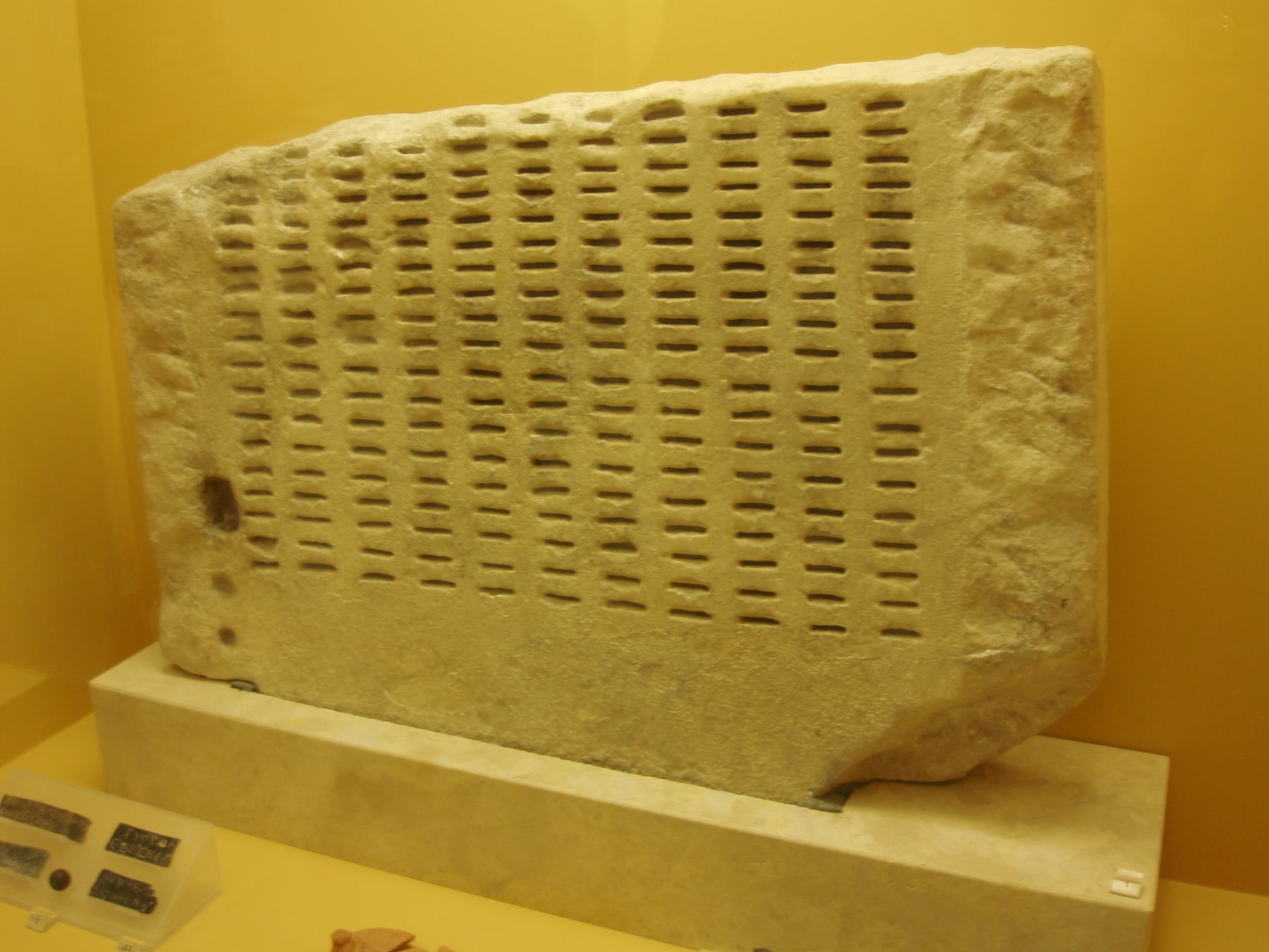 plate A kleroterion in the Stoa of Attalos, Athens. Citizens' tokens were slotted into the columns and a rank of them released at random, so that no faction could arrange who sat. A mechanism for making selection unarguable, cut in stone, two thousand three hundred years before the argument above. Photograph in the public domain.